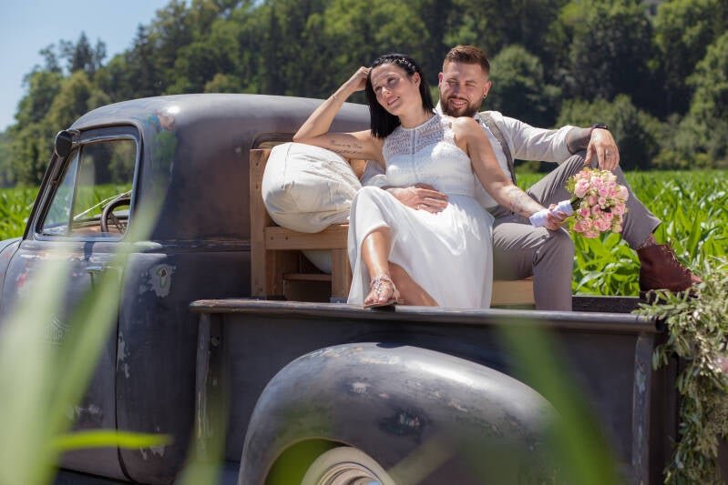 Brautpaar beim Hochzeitsshooting auf einem Vintage-Pickup im Grünen