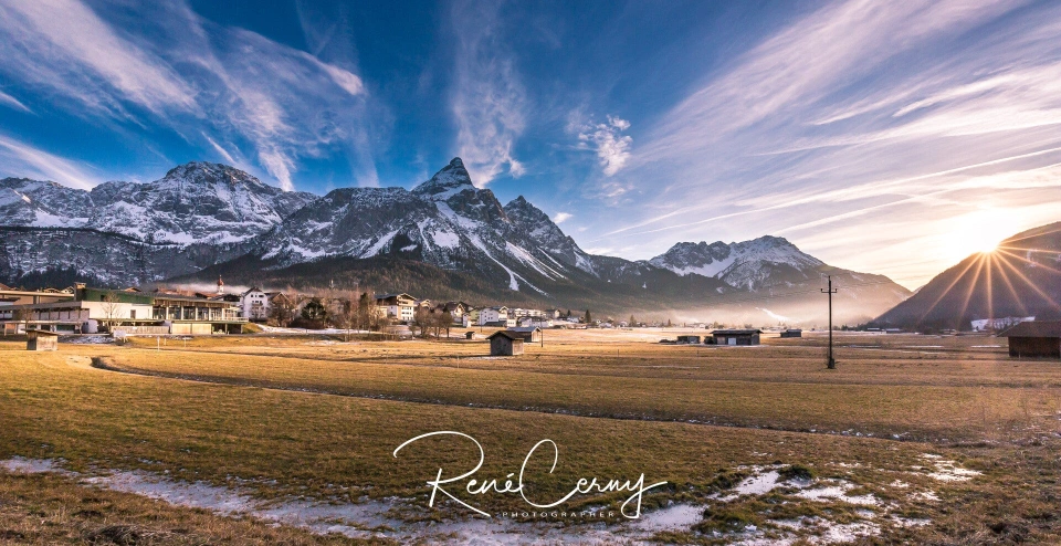 Fotograf René Cerny – Landschaftsfotografie. Alpendorf im Winter bei Sonnenaufgang mit schneebedeckten Gipfeln.