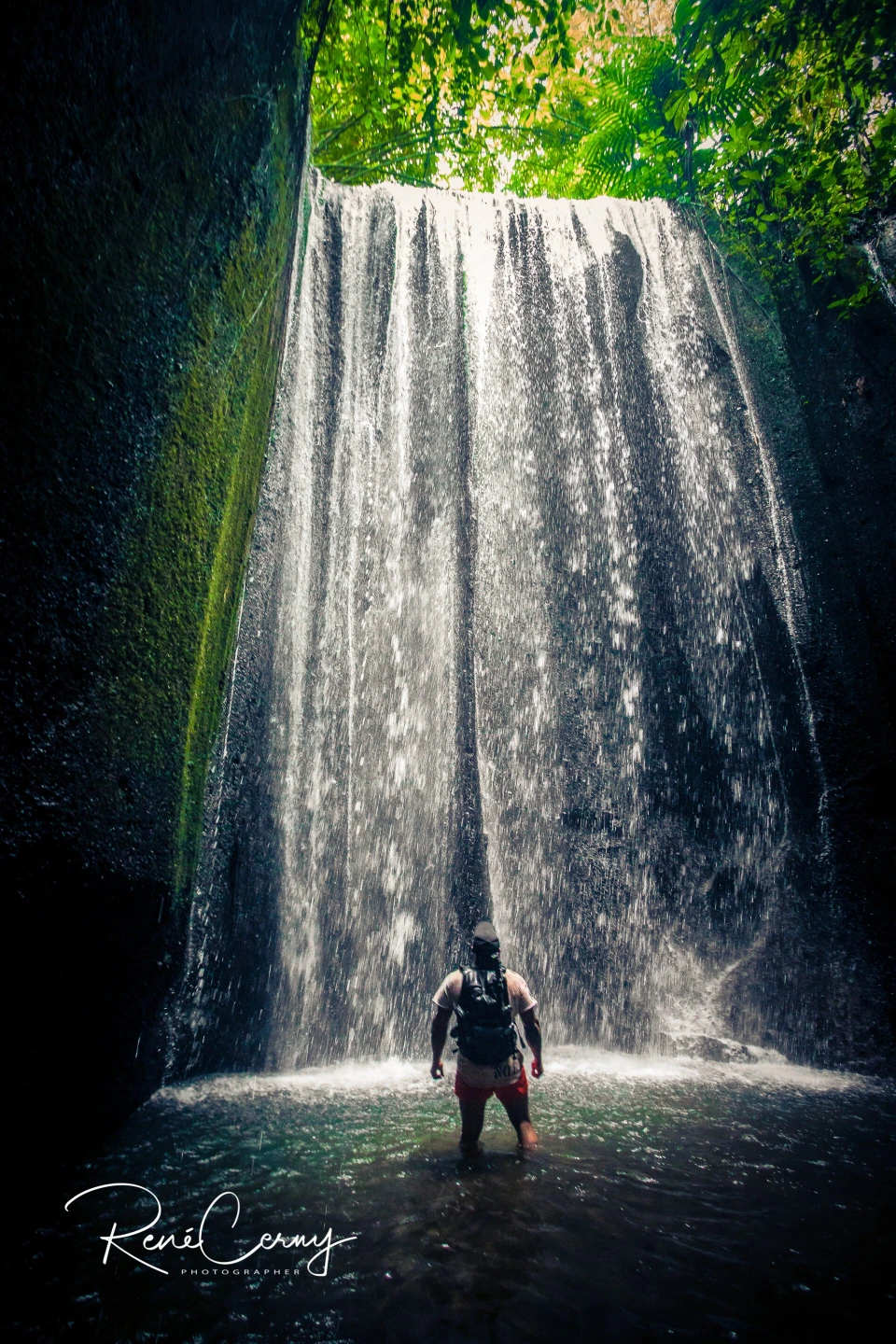 Fotograf René Cerny – Reisefotografie. René steht im Wasserbecken unter einem Dschungel-Wasserfall, Asien.