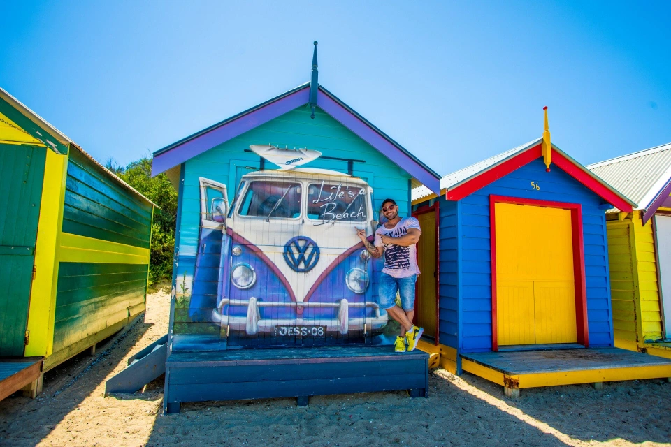 Fotograf René Cerny – Reisefotografie. René posiert vor bunten Strandhütten und einem VW-Bus-Wandbild, Australien.