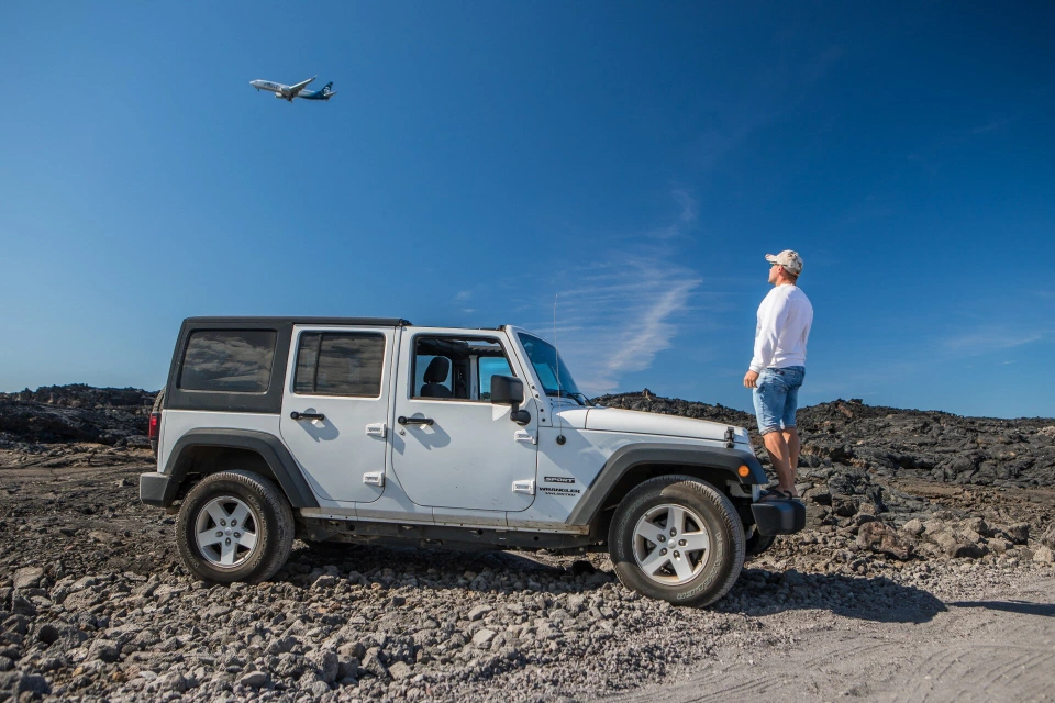 Fotograf René Cerny – Reisefotografie. René beobachtet ein startendes Flugzeug neben einem Jeep im Lavafeld, Hawaii.