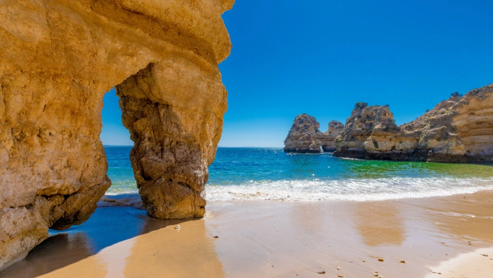 Fotograf René Cerny – Landschaftsfotografie. Felsbogen am Strand mit Blick auf Felsnadeln im Meer, Algarve, Portugal.