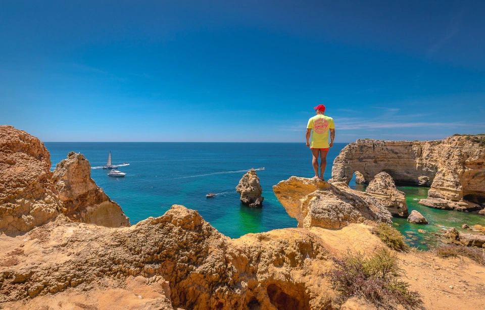 Fotograf René Cerny – Reisefotografie. René steht auf einer Felsklippe mit Blick auf die Bucht, Algarve, Portugal.