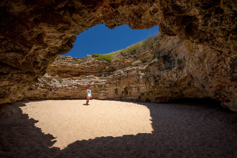 Fotograf René Cerny – Reisefotografie. René steht am Strand im Eingang einer Felsenhöhle, Algarve, Portugal.