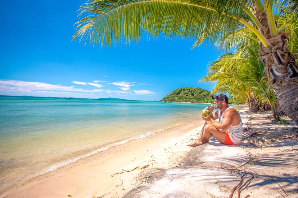 Fotograf René Cerny – Reisefotografie. René trinkt aus einer Kokosnuss am Palmenstrand, Thailand.