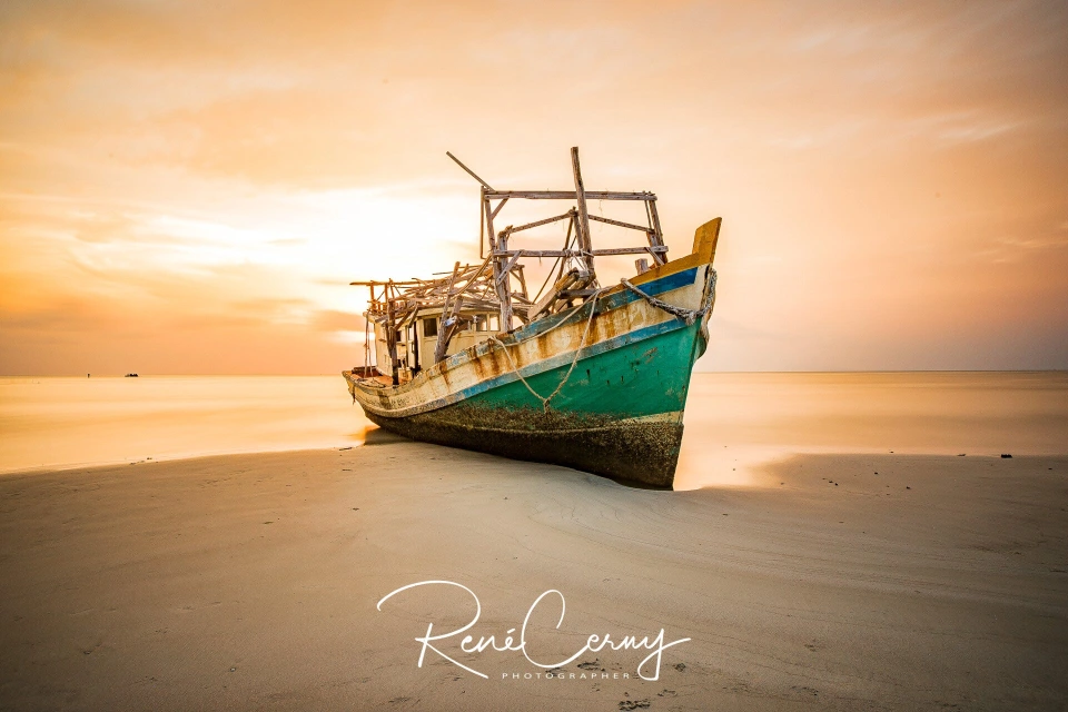 Fotograf René Cerny – Landschaftsfotografie. Gestrandetes hölzernes Fischerboot am Strand bei Sonnenuntergang.
