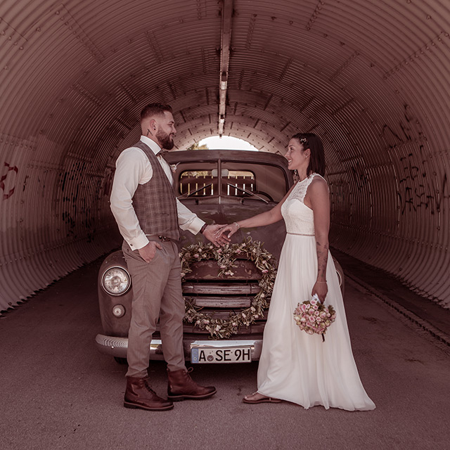Hochzeitsfotograf begleitet das Paar. Pärchen Händchen haltend vor Oldtimer in einem Tunnel
