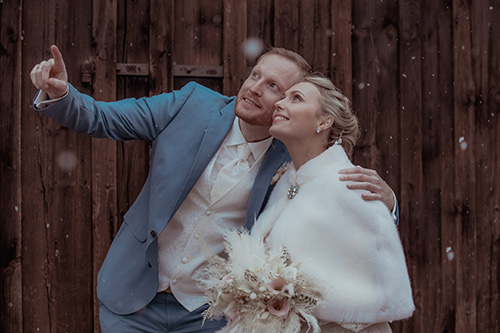 Schöne Hochzeit in Kloster Holzen während es schneit. Brautpaar mit Fotografen René Cerny. Brautpaar posiert vor einer Holzwand